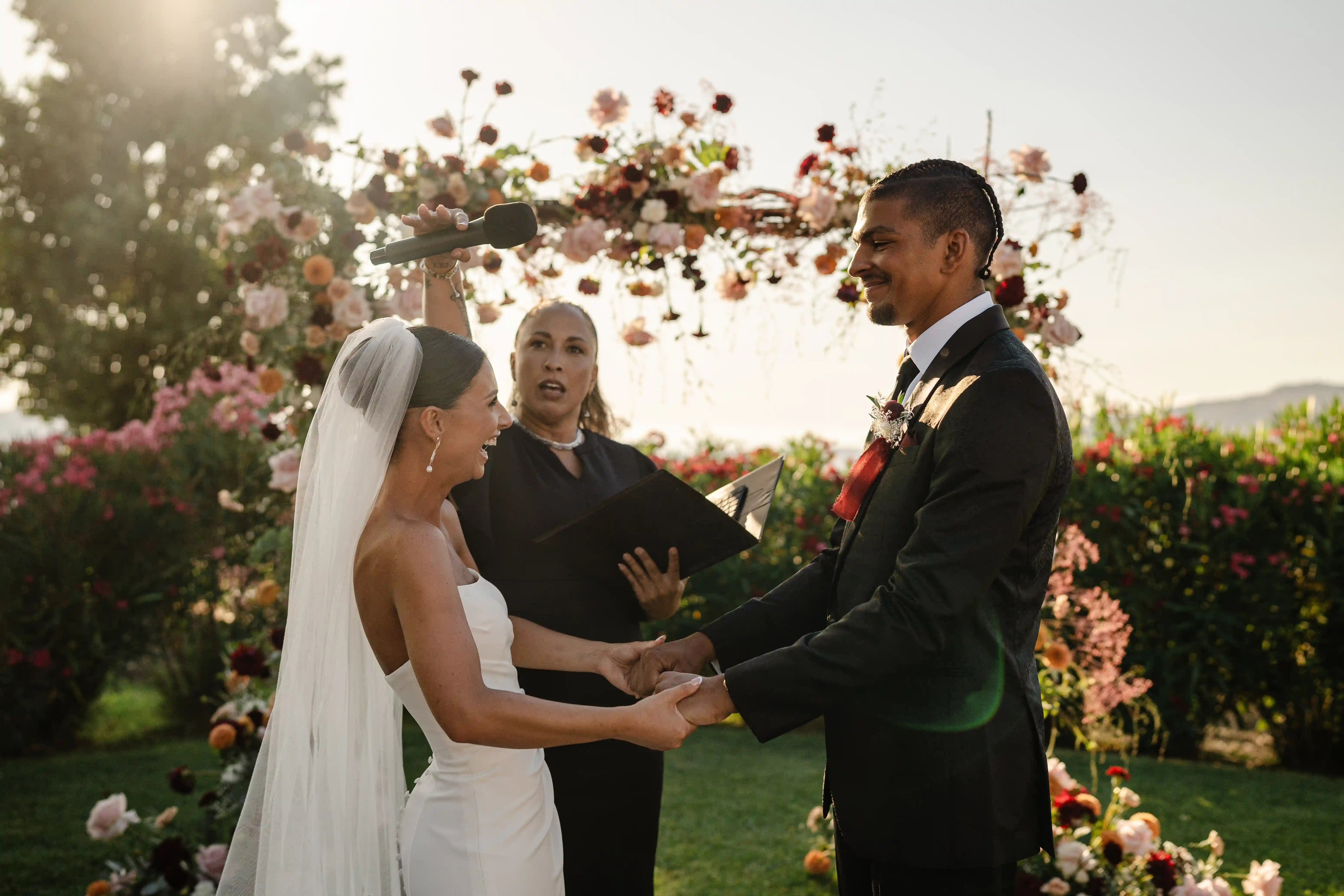 Bride and groom exchanging vows under a floral arch in the warm light of a Sicilian sunset.